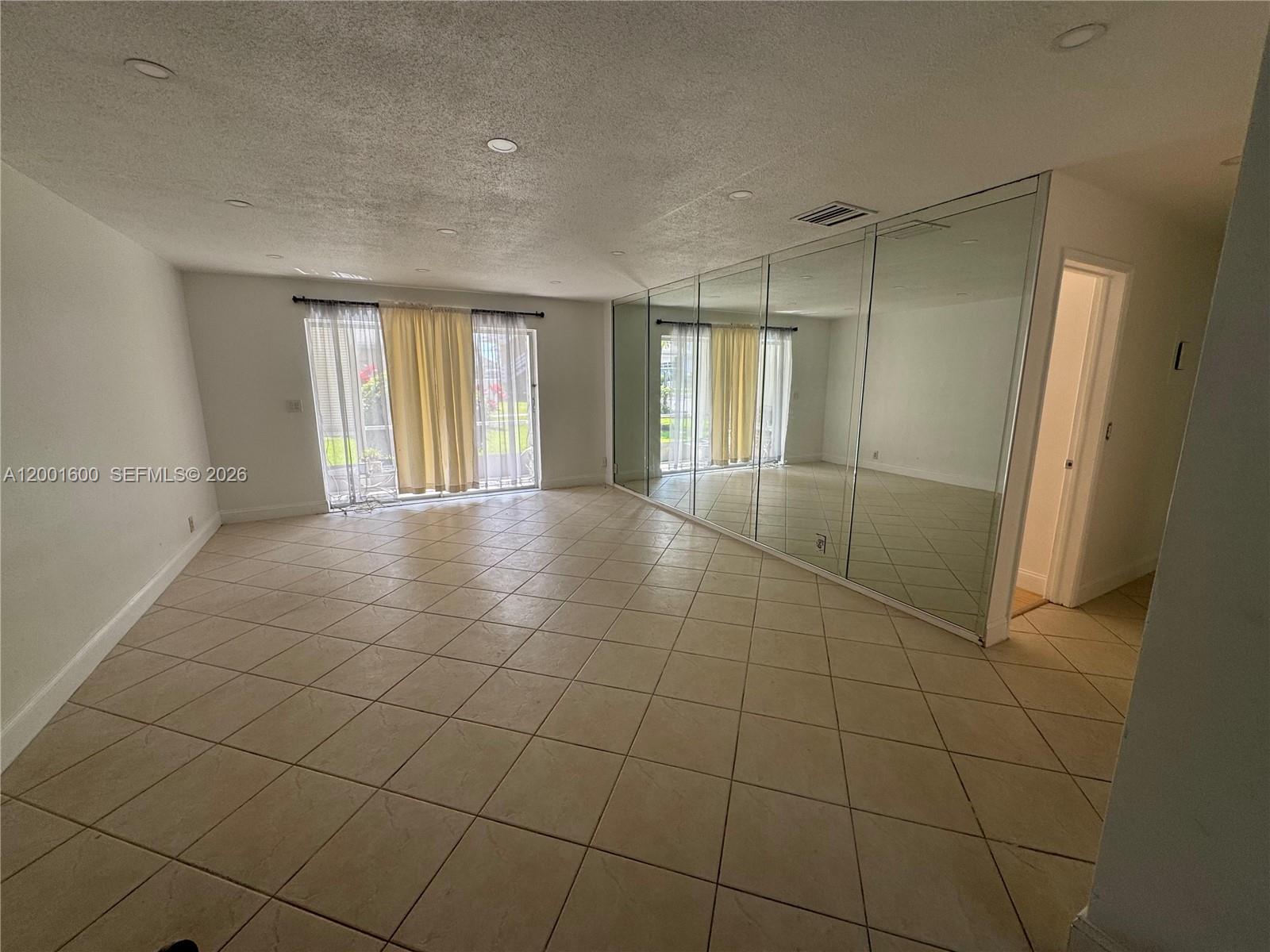 A living room features beige tile flooring, recessed lighting, sliding glass doors, and mirrored walls — 700 Layne Blvd # 115, Hallandale Beach FL 33009, HALLANDALE BEACH, FL