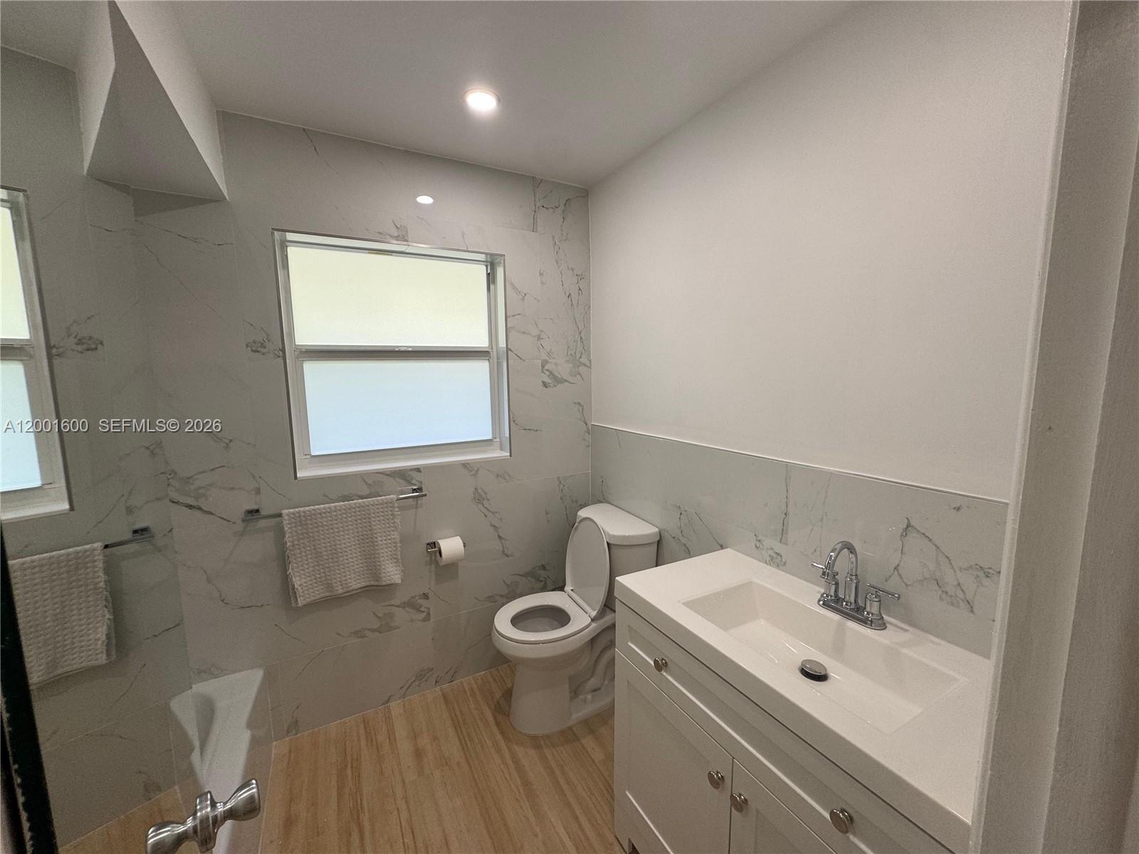 A bathroom features a white vanity, a toilet, and marble-style tile walls — 700 Layne Blvd # 115, Hallandale Beach FL 33009, HALLANDALE BEACH, FL
