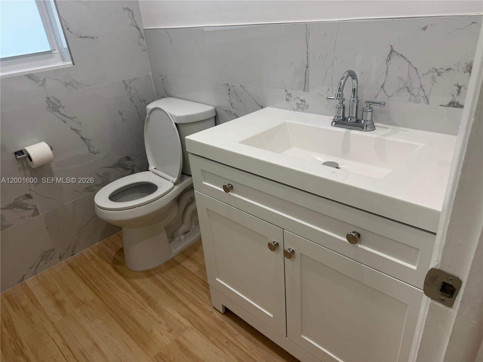 A bathroom features a white vanity, a toilet, and marble-style wall tiles — 700 Layne Blvd # 115, Hallandale Beach FL 33009, HALLANDALE BEACH, FL
