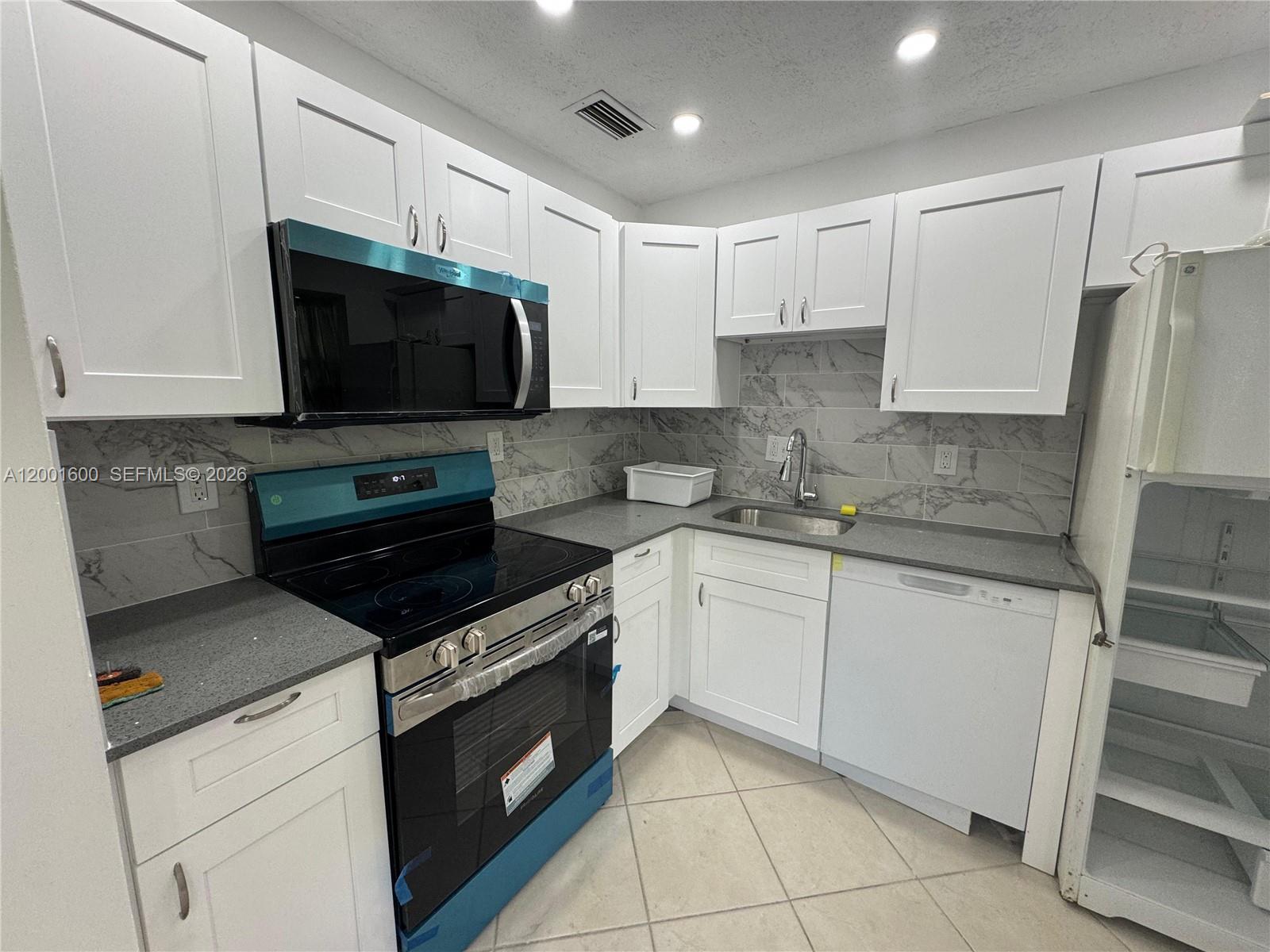 A kitchen features white cabinets, gray countertops, a marble-style backsplash, and stainless steel appliances — 700 Layne Blvd # 115, Hallandale Beach FL 33009, HALLANDALE BEACH, FL