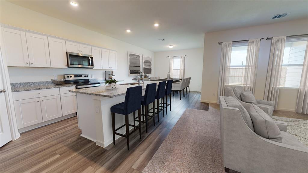 An open-concept kitchen features white cabinets, granite countertops, a center island, and adjacent dining area — 10862 CURVING CREEK LOOP, PARRISH, FL