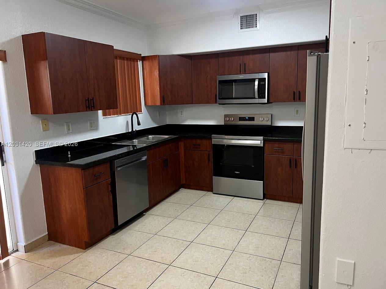 A kitchen features dark wood cabinets, black countertops, and stainless steel appliances over tiled floors — 7281 NW 174th Ter # 103, Hialeah FL 33015, HIALEAH, FL