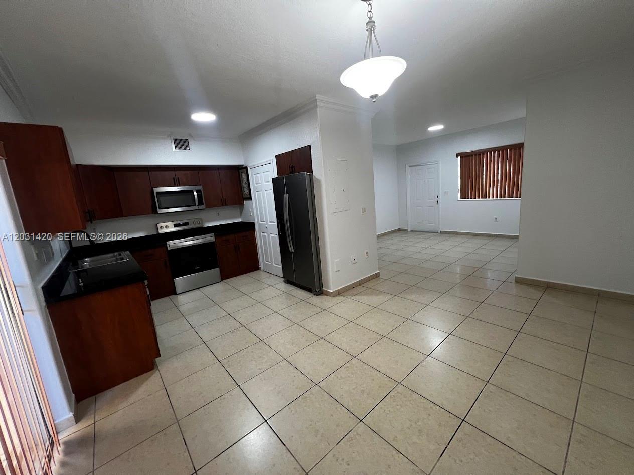 A kitchen with dark wood cabinets and stainless steel appliances opens into a tiled living area — 7281 NW 174th Ter # 103, Hialeah FL 33015, HIALEAH, FL