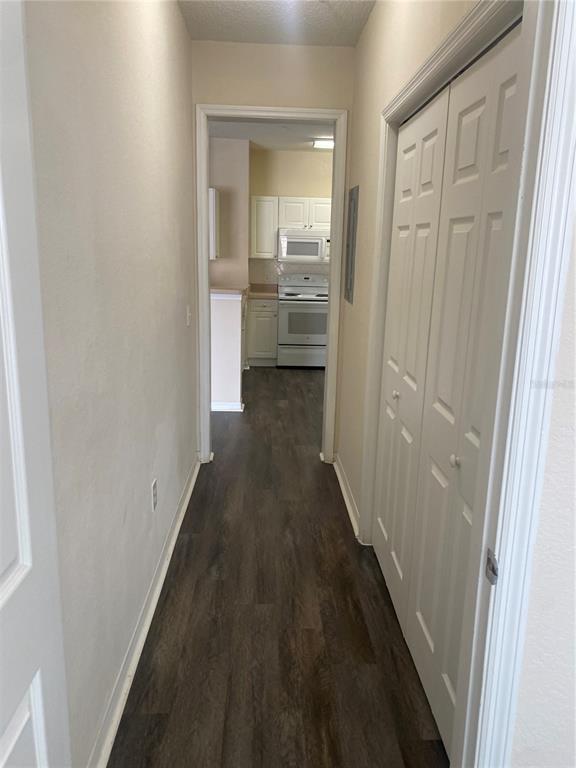 A hallway with dark wood-look flooring leads to a kitchen with white cabinets and appliances — 18001 RICHMOND PLACE DRIVE UNIT 222, TAMPA, FL