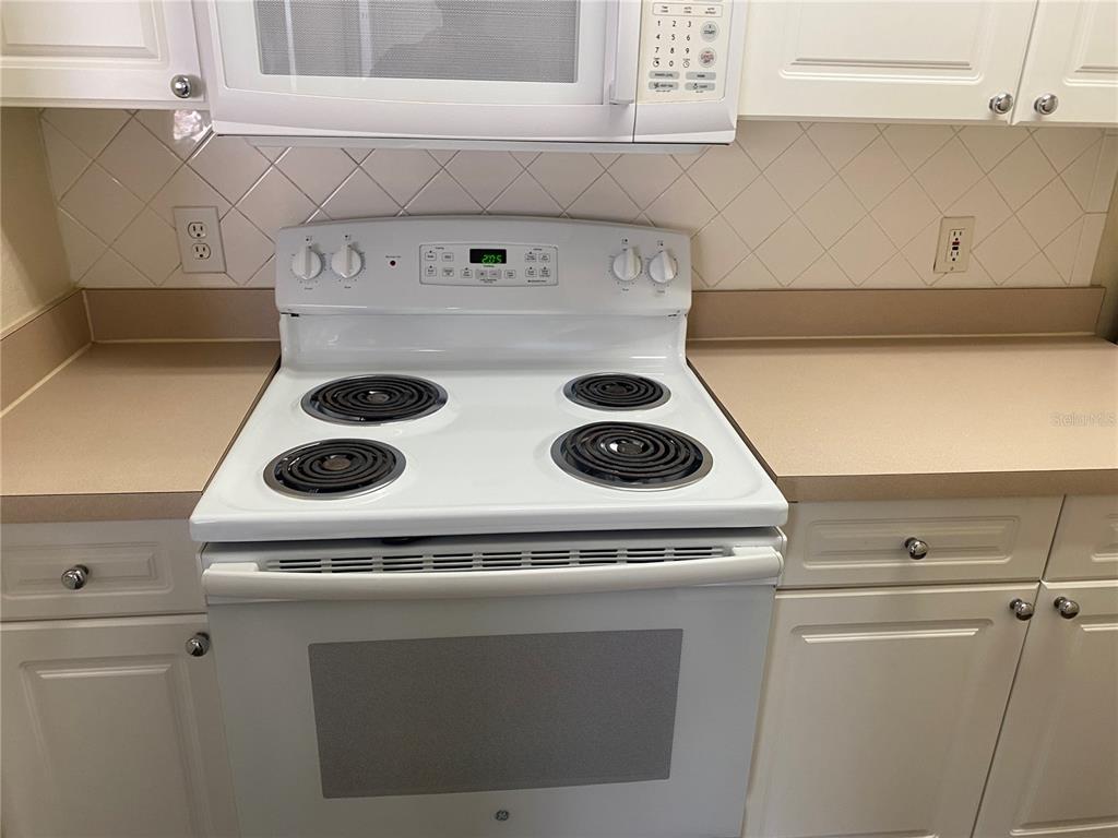 A white electric stove and microwave are installed between white cabinets and a tile backsplash — 18001 RICHMOND PLACE DRIVE UNIT 222, TAMPA, FL