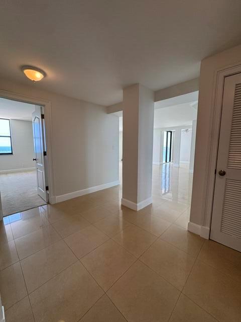 A bright hallway with beige tile flooring leads to an open living area with windows — 1000 S Ocean Boulevard # 14a, Pompano Beach FL 33062, POMPANO BEACH, FL