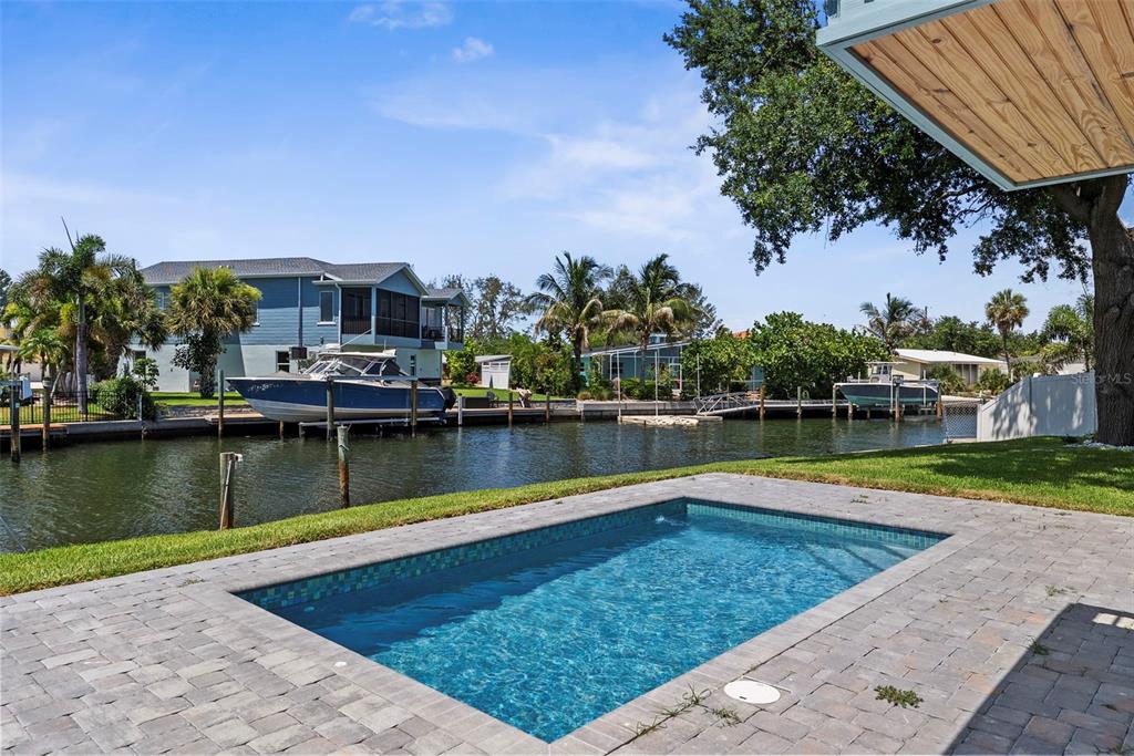 A backyard swimming pool overlooks a canal with docked boats and waterfront homes — 10016 KINGFISHER ROAD E, BRADENTON, FL