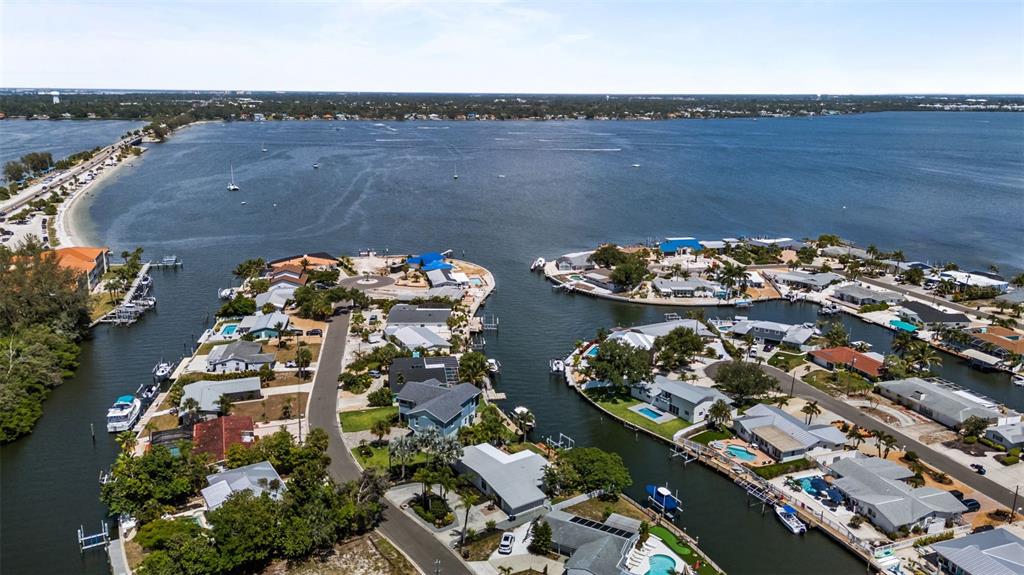 An aerial view shows waterfront houses with private docks along a canal and bay — 10016 KINGFISHER ROAD E, BRADENTON, FL
