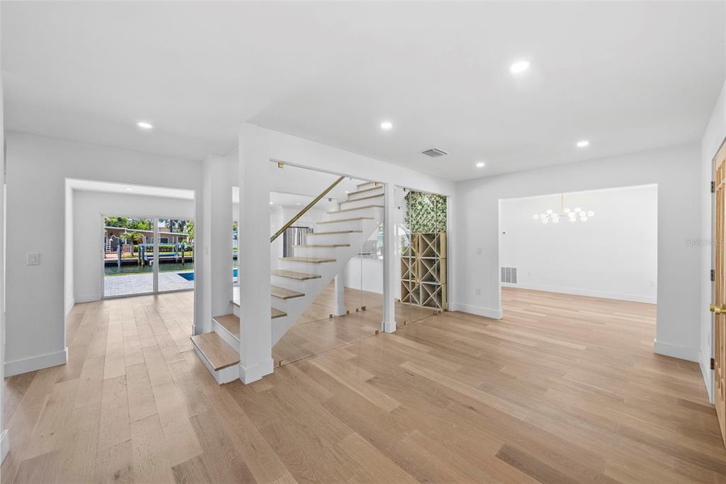 A bright, modern room features light wood floors, a floating staircase, and a glass-enclosed wine rack — 10016 KINGFISHER ROAD E, BRADENTON, FL