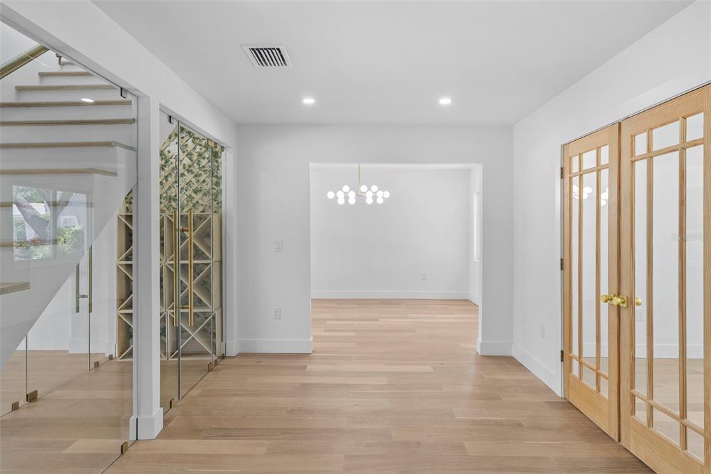 A bright entryway features light wood flooring, a glass-enclosed wine cellar, and double French doors — 10016 KINGFISHER ROAD E, BRADENTON, FL