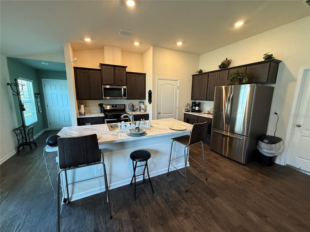 A kitchen features dark wood cabinets, a marble-topped island with stools, and stainless steel appliances — 13 PINNACLE PLACE, BUNNELL, FL