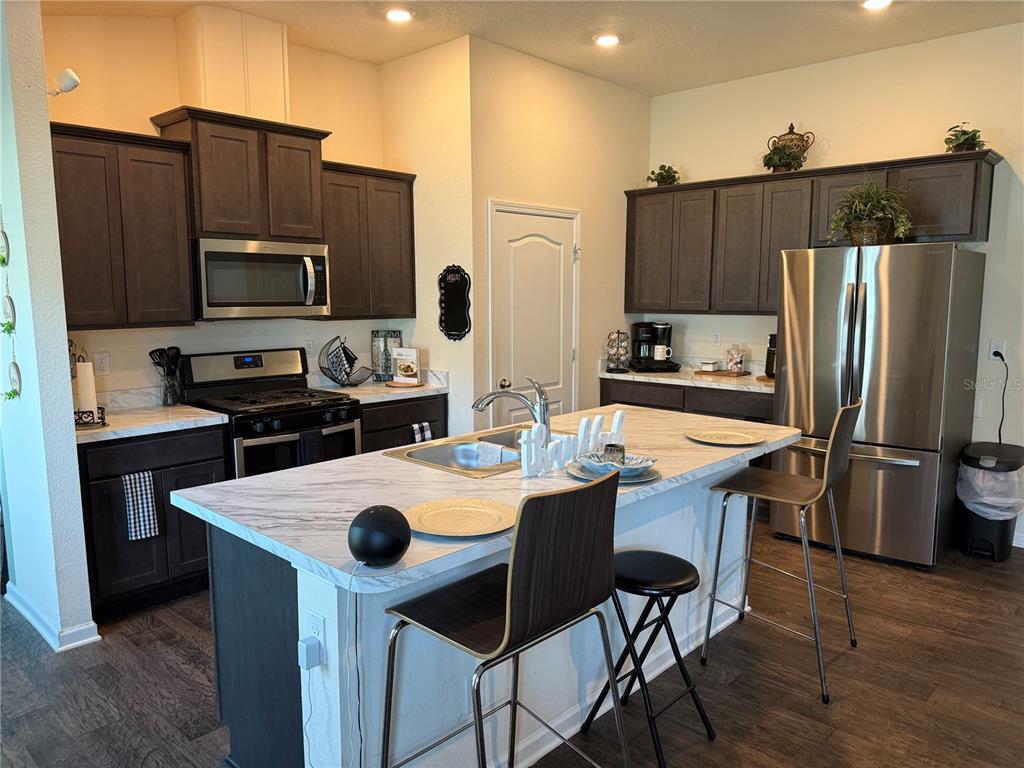 A kitchen features dark wood cabinets, stainless steel appliances, and a marble-patterned island countertop — 13 PINNACLE PLACE, BUNNELL, FL