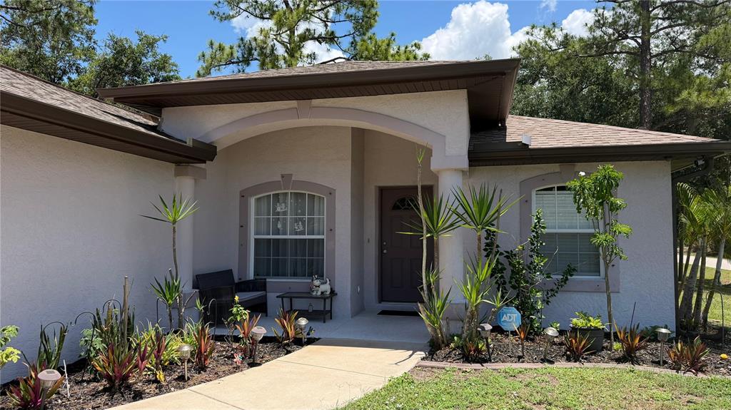 The exterior of a single-story home features a covered entryway, stucco walls, and landscaping — 2204 SPARKLE LANE, NORTH PORT, FL
