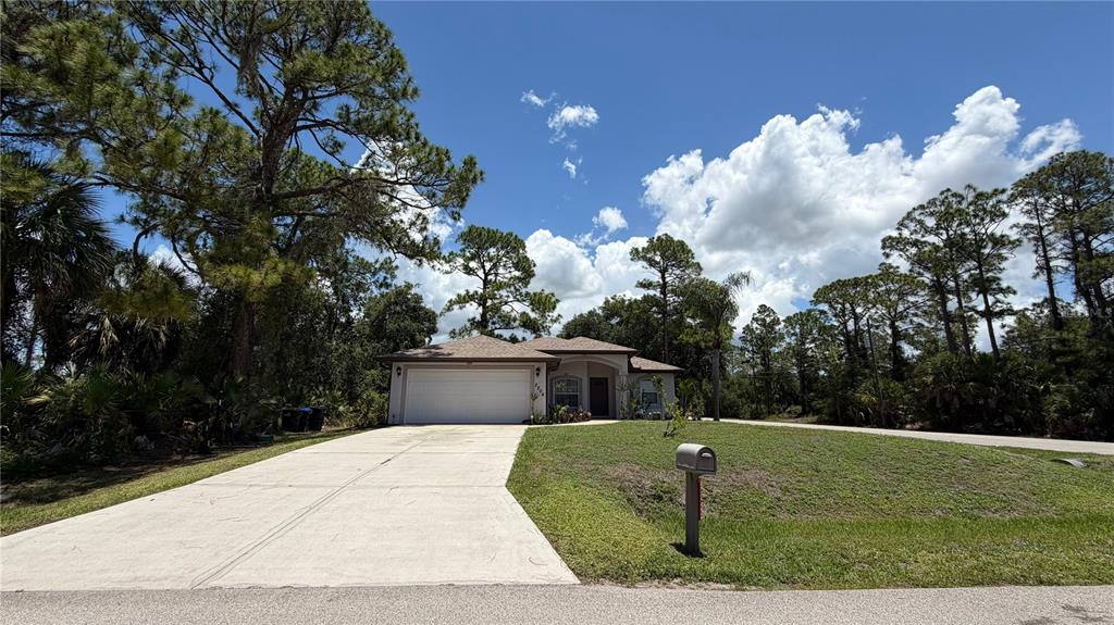 A single-story house with a white garage door and a concrete driveway sits among trees — 2204 SPARKLE LANE, NORTH PORT, FL