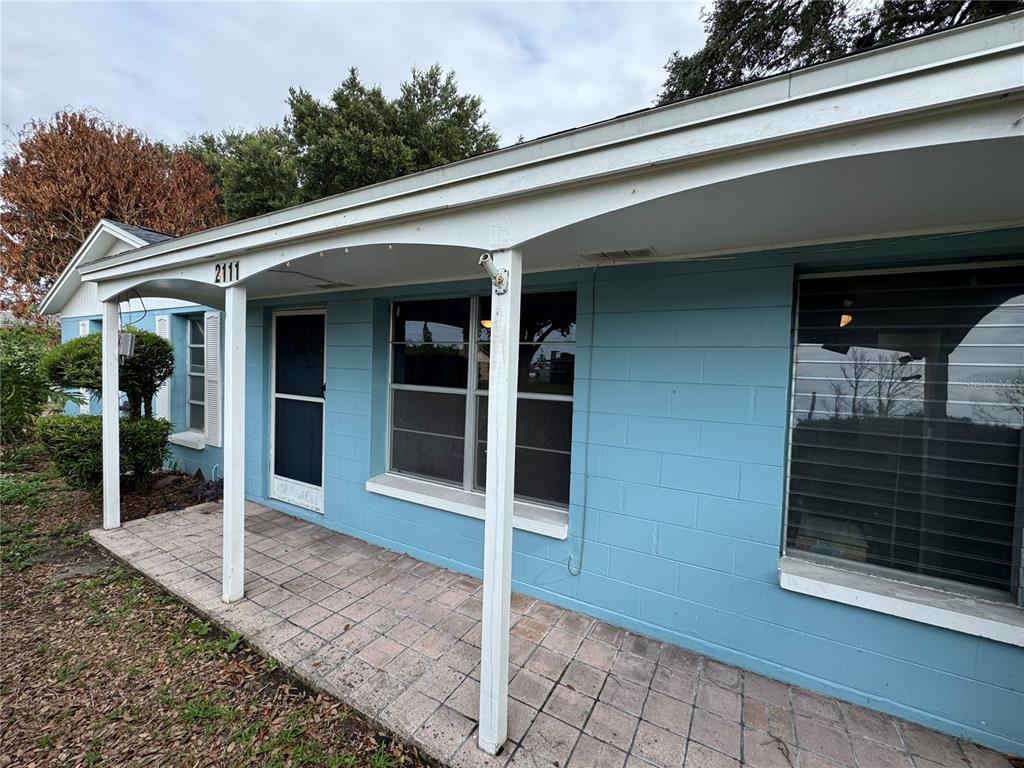 A blue concrete block house features a covered front porch with white support posts — 2111 S CRYSTAL LAKE DRIVE, LAKELAND, FL
