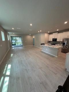 An open-concept kitchen and living area features light wood-look flooring and white cabinetry — 3490 TIMBER CROSSING AVENUE, BRANDON, FL