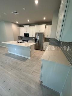 A modern kitchen features white cabinetry, a central island, and light-colored wood-look flooring — 3490 TIMBER CROSSING AVENUE, BRANDON, FL