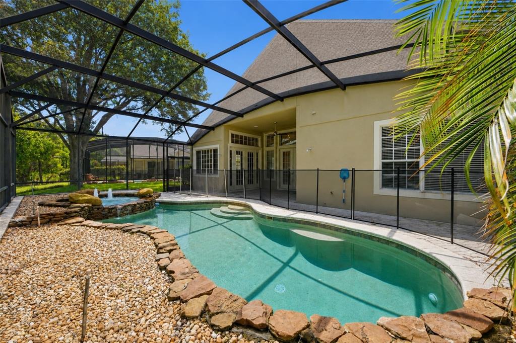 A screened-in patio features a swimming pool with a rock border and an attached spa — 11027 SUMMERSPRING LAKES DRIVE, ORLANDO, FL