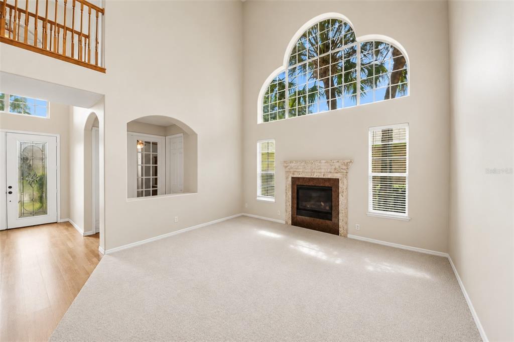 A living room with high ceilings, a fireplace, carpeted floors, and a large arched window — 11027 SUMMERSPRING LAKES DRIVE, ORLANDO, FL