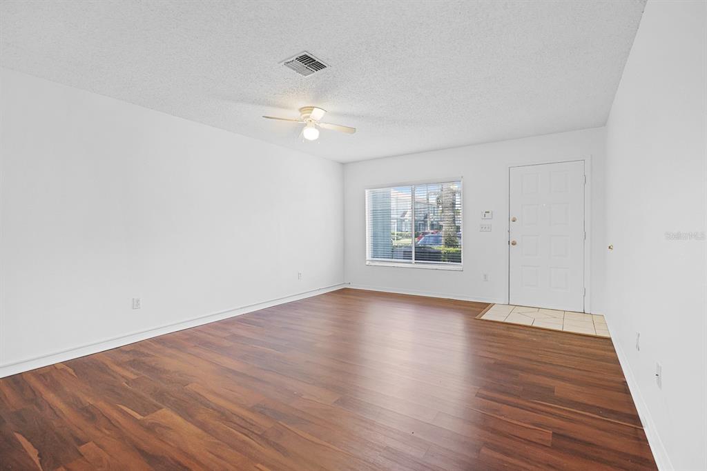 An empty room features white walls, dark wood-look flooring, a ceiling fan, and a front door — 1326 TWILRIDGE PLACE, BRANDON, FL