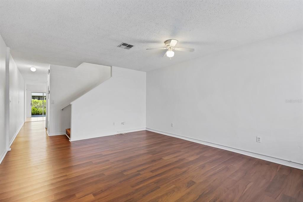 An empty living room features wood-look flooring, white walls, a ceiling fan, and a staircase — 1326 TWILRIDGE PLACE, BRANDON, FL