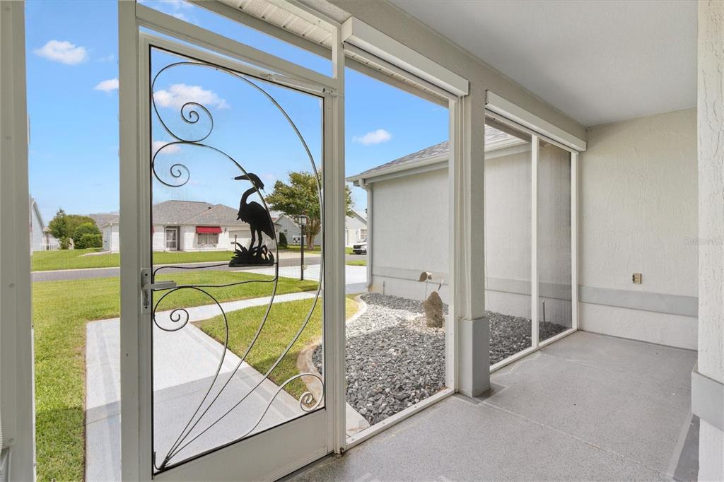 A screened-in porch features a decorative metal door with a heron design and gravel landscaping — 811 SAN SALVADOR DRIVE, THE VILLAGES, FL