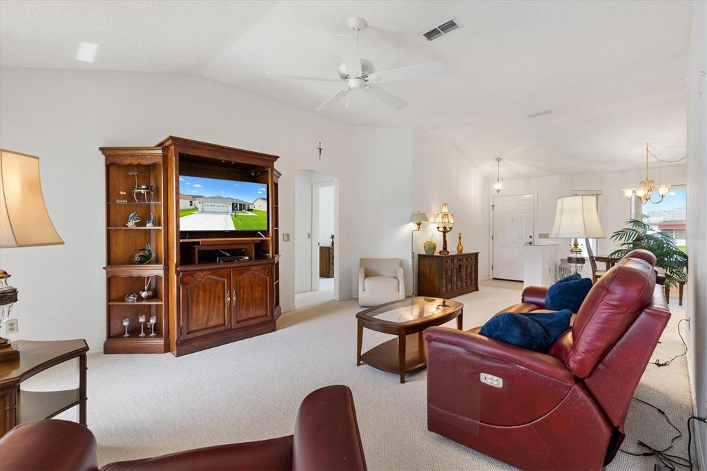 A living room features a large wooden entertainment center, red leather recliners, and carpeted floors — 811 SAN SALVADOR DRIVE, THE VILLAGES, FL