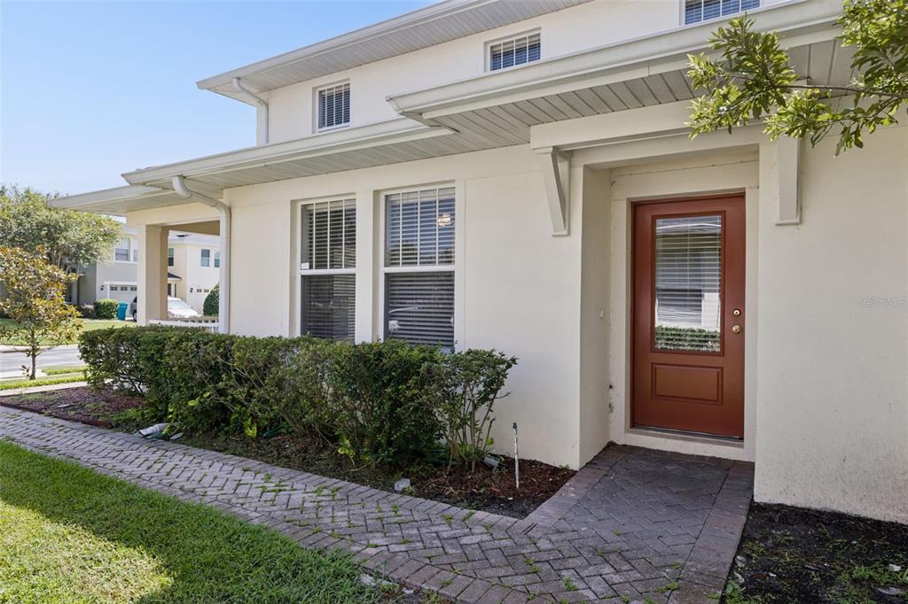 A cream-colored house exterior features a red front door, brick walkway, and manicured hedges — 5408 CARAMELLA DRIVE, ORLANDO, FL