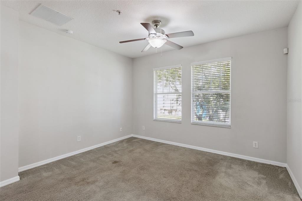 An empty bedroom features light gray walls, beige carpeting, two windows, and a ceiling fan — 5408 CARAMELLA DRIVE, ORLANDO, FL