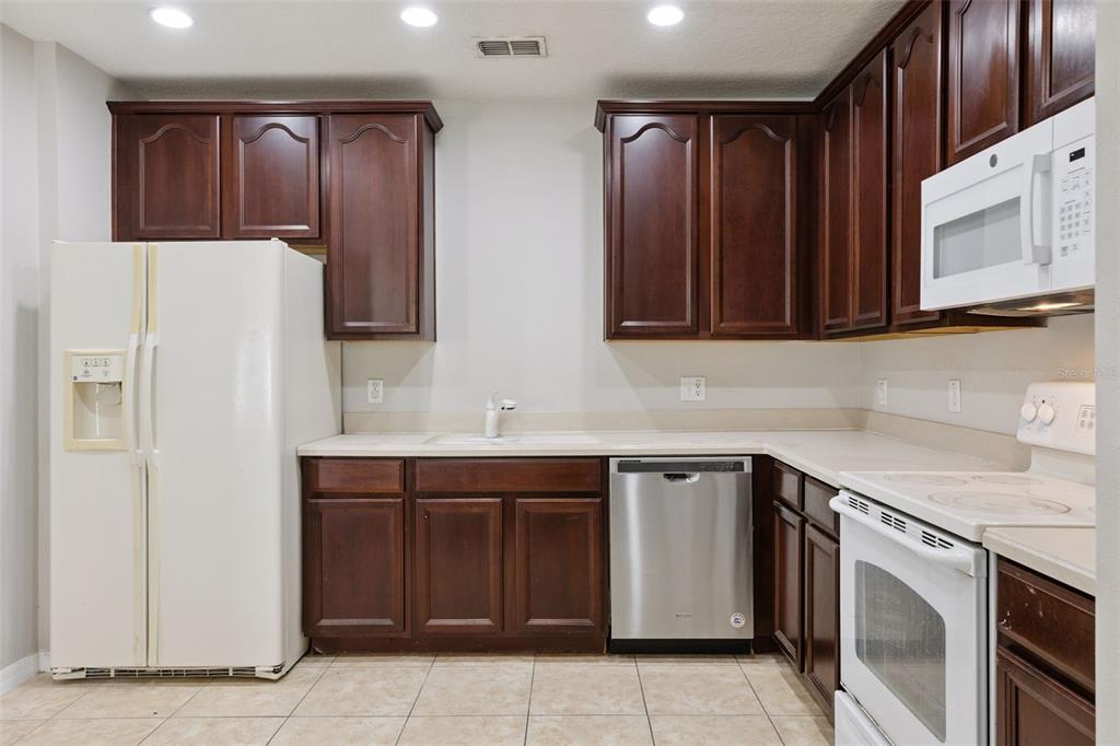 A kitchen features dark wood cabinets, white appliances, a stainless steel dishwasher, and tile flooring — 5408 CARAMELLA DRIVE, ORLANDO, FL