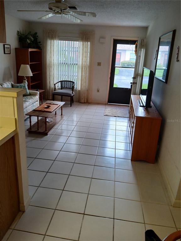 A living room features white tile flooring, a ceiling fan, and a glass-paneled entry door — 6050 CHESHAM DRIVE UNIT 3, NEW PORT RICHEY, FL