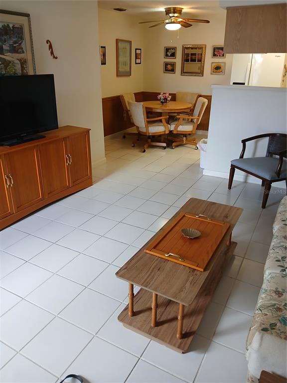 A living room with white tile floors, a wooden media console, and a dining area — 6050 CHESHAM DRIVE UNIT 3, NEW PORT RICHEY, FL