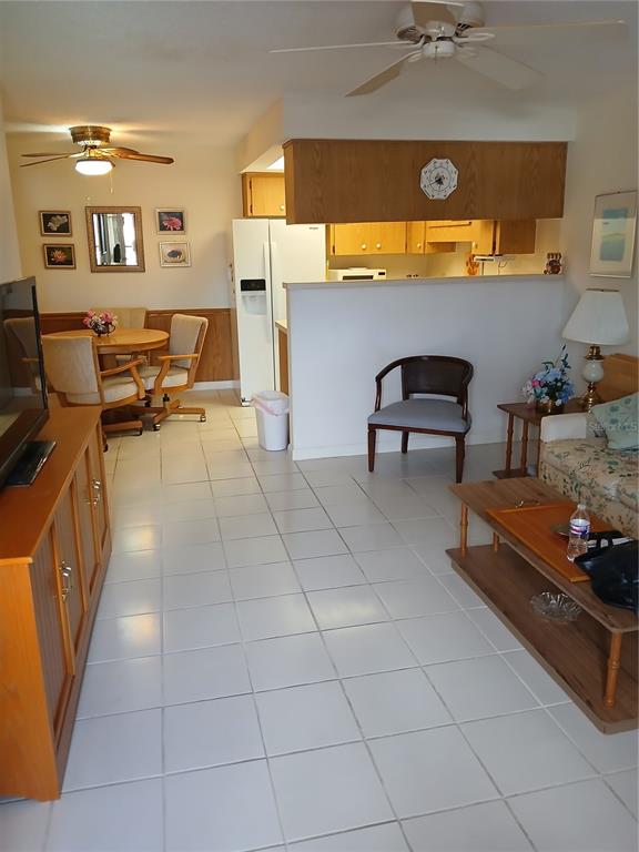An open-concept living and dining area features white tile floors, wood cabinetry, and ceiling fans — 6050 CHESHAM DRIVE UNIT 3, NEW PORT RICHEY, FL