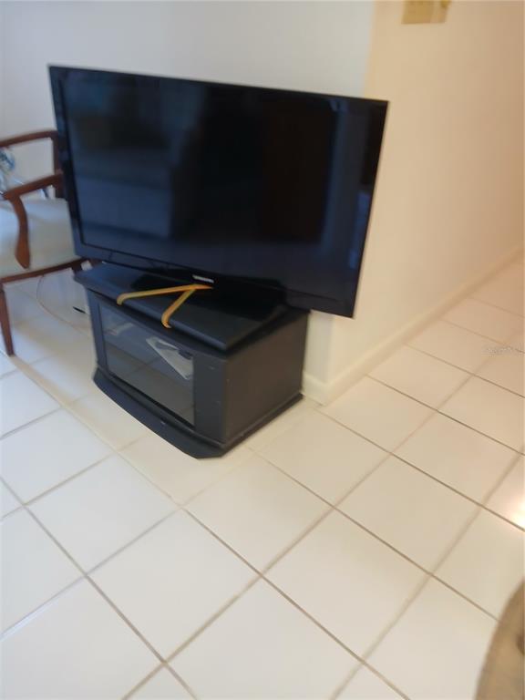 A television sits on a black media console in a room with white tiled flooring — 6050 CHESHAM DRIVE UNIT 3, NEW PORT RICHEY, FL