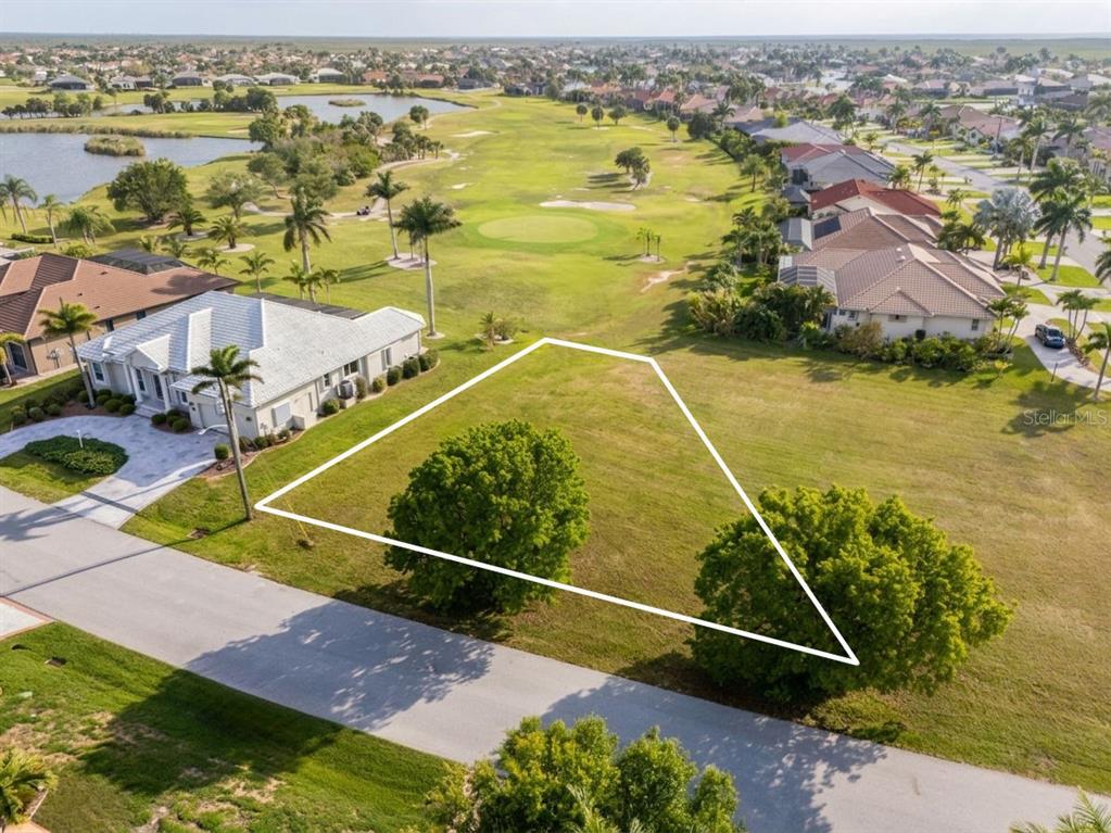 An aerial view shows a vacant, trapezoidal residential lot situated next to a house and golf course — 3707 BORDEAUX DRIVE, PUNTA GORDA, FL