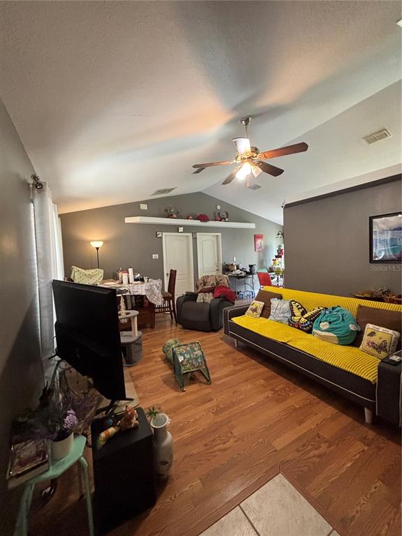 A living room features wood-look flooring, a vaulted ceiling with a fan, and a yellow sofa — 4250 WORTHINGTON PLACE, MASCOTTE, FL