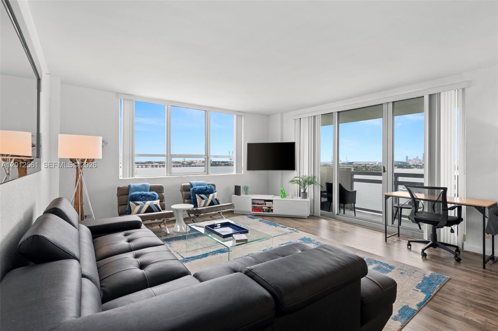 A living room features a dark sectional sofa, glass coffee table, and floor-to-ceiling water views — 1500 Bay Rd # 1438S, Miami Beach FL 33139, MIAMI BEACH, FL