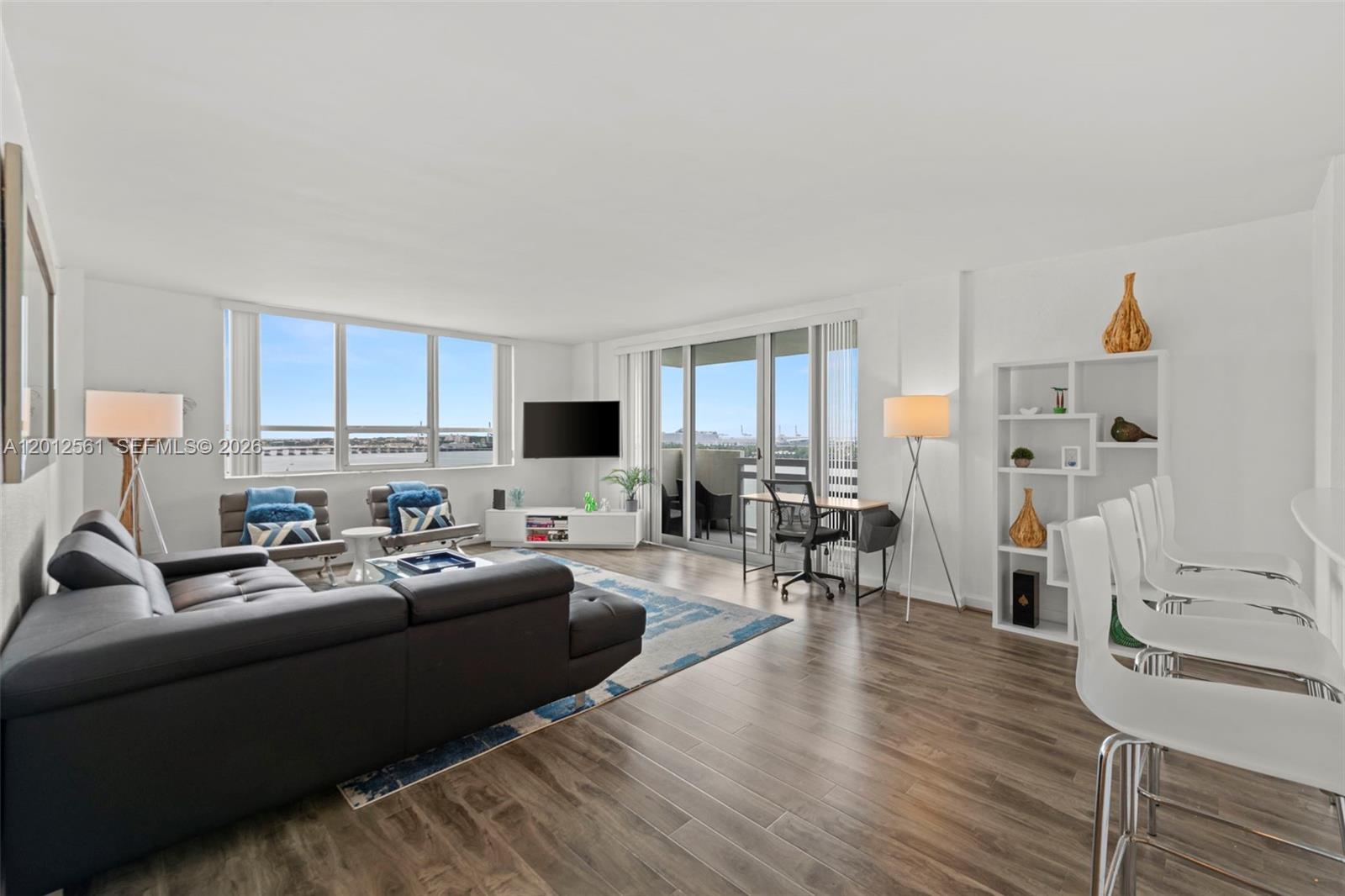 A modern living room features a dark sectional sofa, wood-look flooring, and floor-to-ceiling windows — 1500 Bay Rd # 1438S, Miami Beach FL 33139, MIAMI BEACH, FL