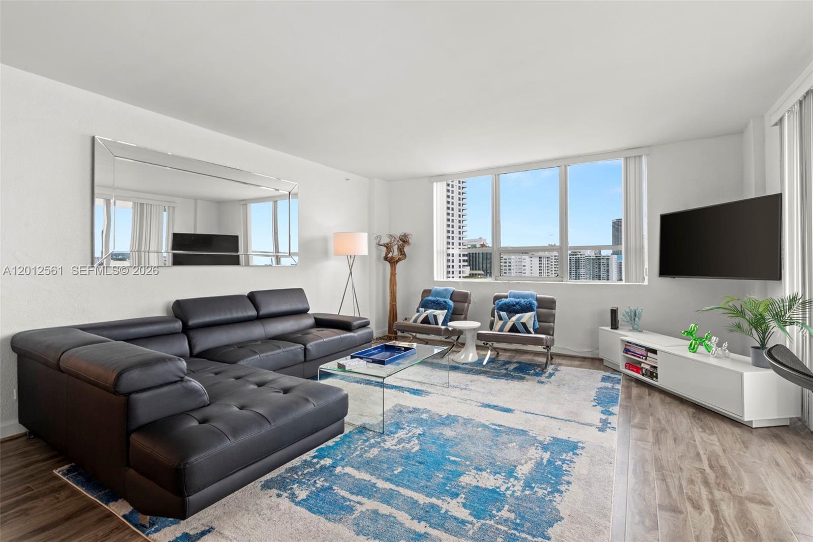 A living room features a black sectional sofa, a blue patterned rug, and large windows — 1500 Bay Rd # 1438S, Miami Beach FL 33139, MIAMI BEACH, FL