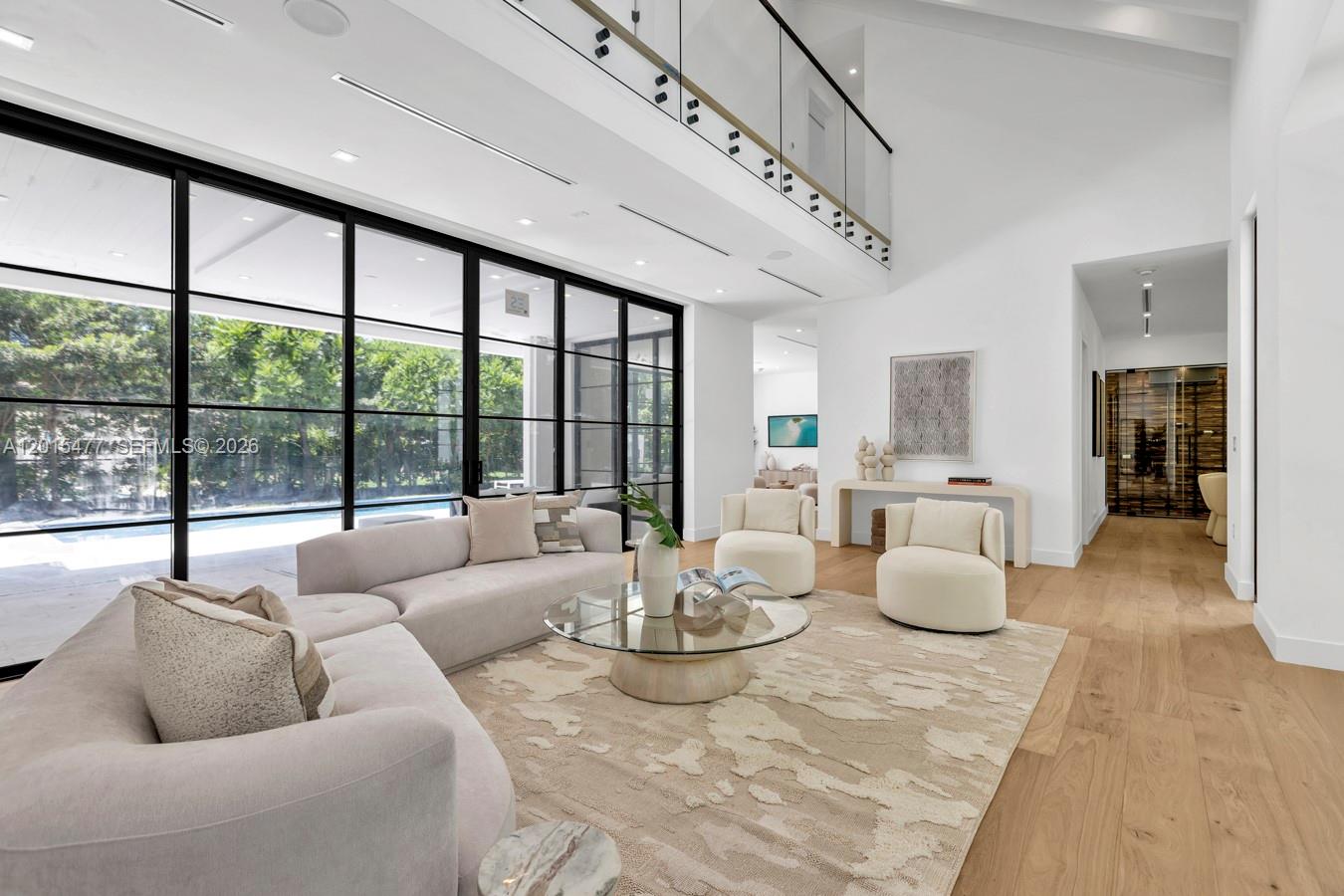 A bright, modern living room features a double-height ceiling, glass walls, and light wood floors — 1220 S Alhambra Cir, Coral Gables FL 33146, CORAL GABLES, FL