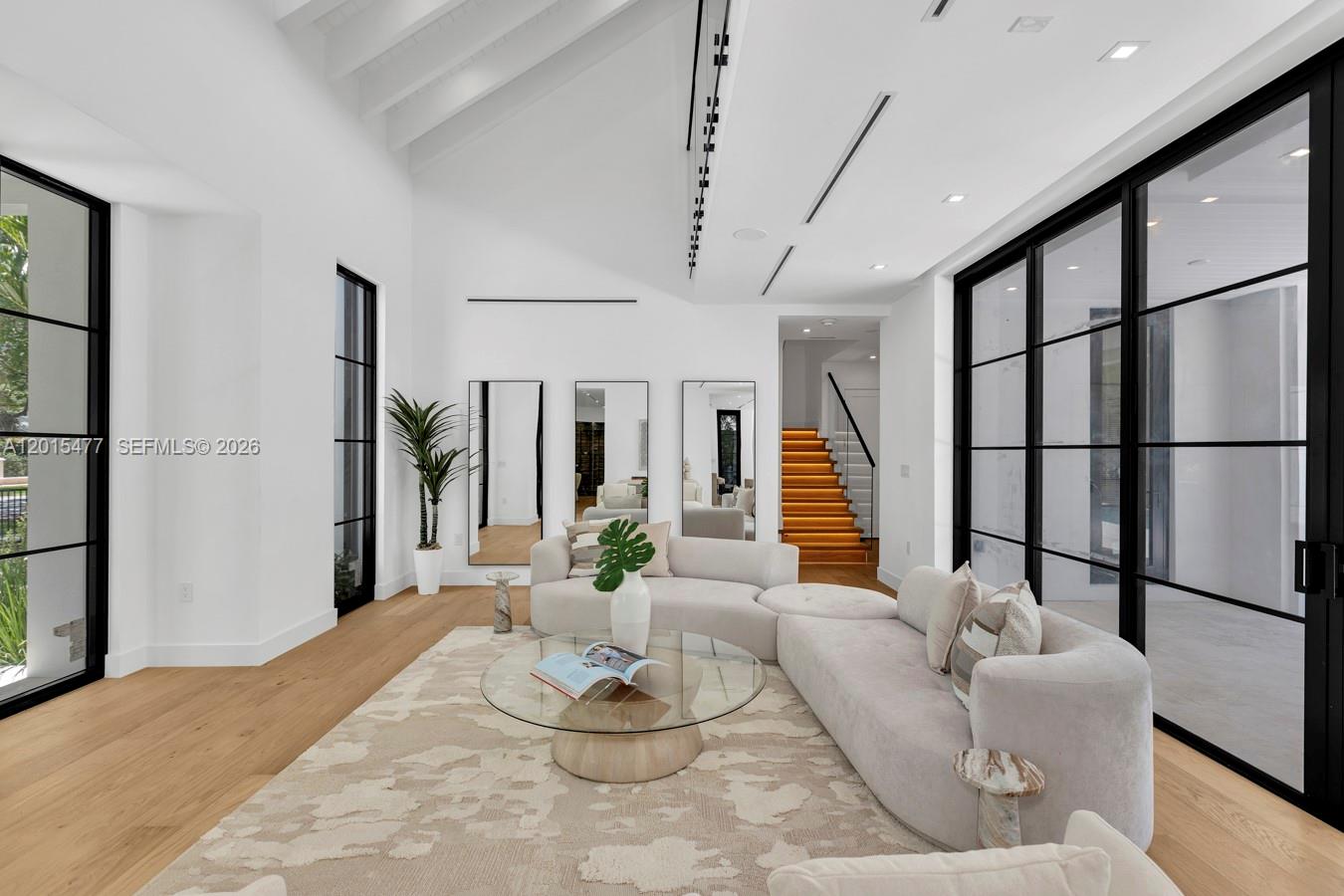 A modern living room features white walls, light wood floors, and large black-framed glass doors — 1220 S Alhambra Cir, Coral Gables FL 33146, CORAL GABLES, FL