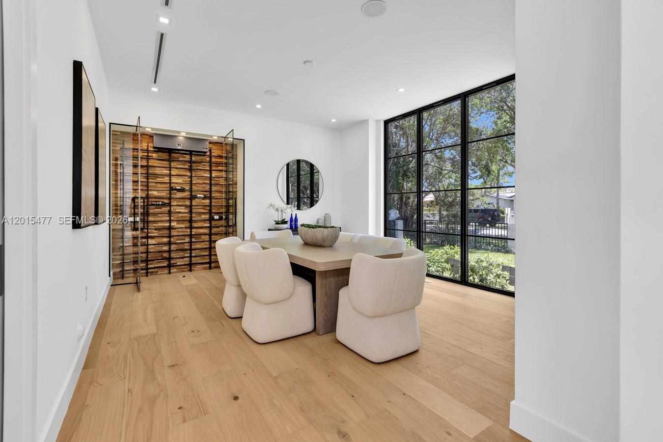 A dining room features a wood-paneled wine wall, light hardwood floors, and large black-framed windows — 1220 S Alhambra Cir, Coral Gables FL 33146, CORAL GABLES, FL
