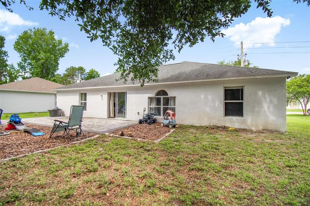 The backyard of a white house features a paved patio, a lawn, and children's toys — 195 PARKVIEW DRIVE, PALM COAST, FL