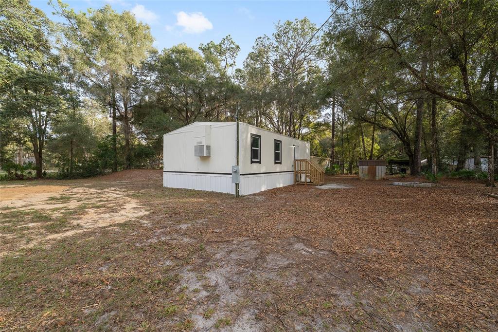 A white mobile home sits on a wooded lot with a small wooden staircase — 1630 SE 178TH LANE, SUMMERFIELD, FL
