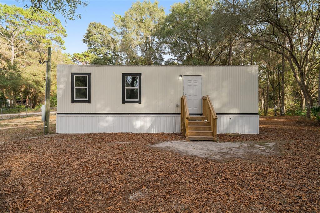 A single-story mobile home with white siding, two windows, and wooden stairs sits outdoors — 1630 SE 178TH LANE, SUMMERFIELD, FL