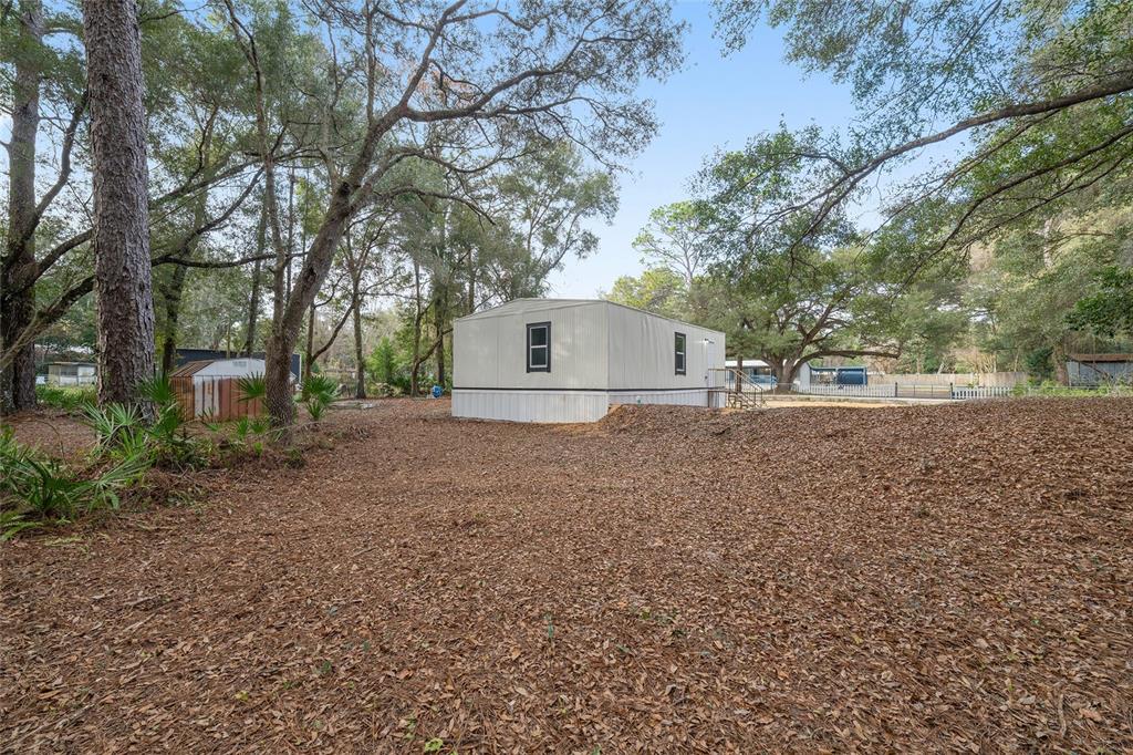 A mobile home sits on a leaf-covered lot surrounded by large trees — 1630 SE 178TH LANE, SUMMERFIELD, FL