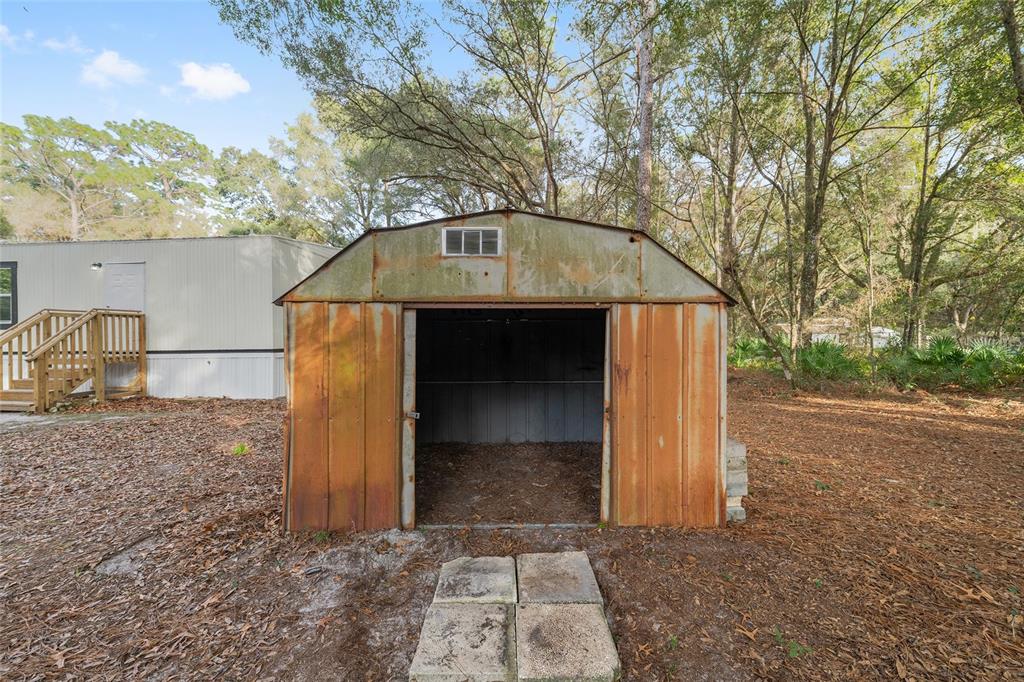 A weathered, rusted metal storage shed stands in a wooded yard next to a mobile home — 1630 SE 178TH LANE, SUMMERFIELD, FL