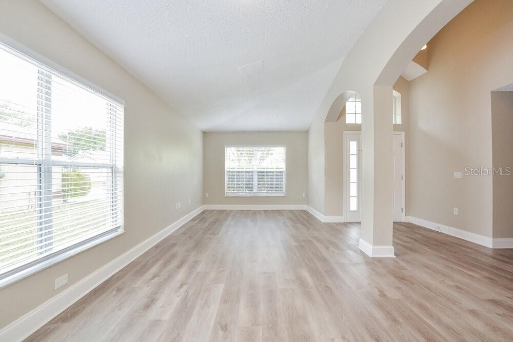 An empty living room features light-colored wood-look flooring, neutral walls, and large windows — 8344 LAKE AMHURST TRAIL, ORLANDO, FL