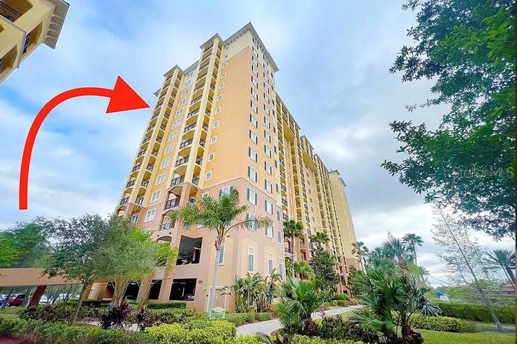 A low-angle exterior view of a tall, yellow multi-story residential building with a red arrow — 8125 RESORT VILLAGE DRIVE UNIT 51201, ORLANDO, FL