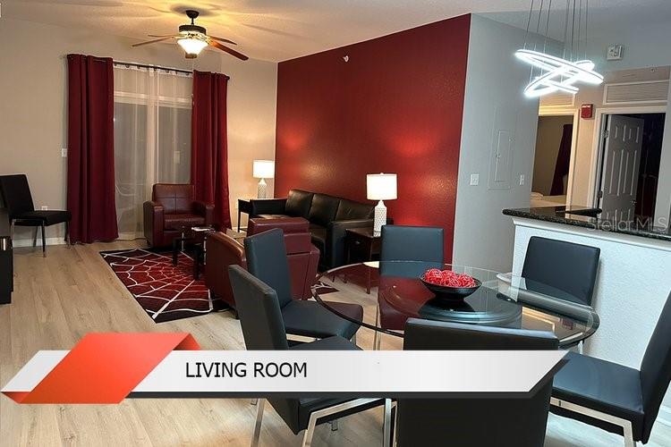 A living room and dining area feature wood-look flooring, a red accent wall, and furniture — 8125 RESORT VILLAGE DRIVE UNIT 51201, ORLANDO, FL